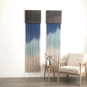 May include: Two wall hangings featuring rectangular dark brown wooden tops with long, vertical fiber strands that transition in color from deep navy blue at the top to light teal and finally to a natural off-white cream color at the bottom.