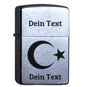 Op de afbeelding: Een zilveren aansteker met een zwart halve maan- en sterontwerp. De aansteker heeft een zwarte rand en de tekst "Dein Text" is gegraveerd op de voor- en achterkant.