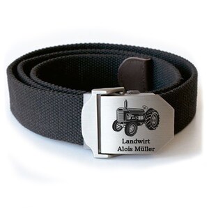 Op de afbeelding: Een zwarte canvas riem met een zilveren gesp. De gesp is gegraveerd met een afbeelding van een tractor en de tekst "Landwirt Alois M&uuml;ller".