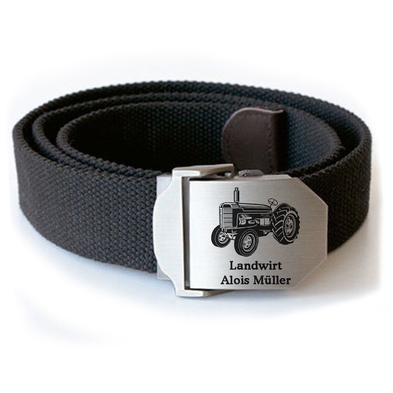 Op de afbeelding: Een zwarte canvas riem met een zilveren gesp. De gesp is gegraveerd met een afbeelding van een tractor en de tekst "Landwirt Alois M&uuml;ller".