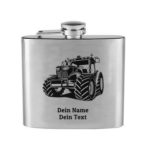 Op de afbeelding: Een zilveren roestvrijstalen hipflask met een zwart-witte illustratie van een tractor. De fles heeft een scharnierende dop en de tekst "Dein Name Dein Text" is gegraveerd op de voorkant.