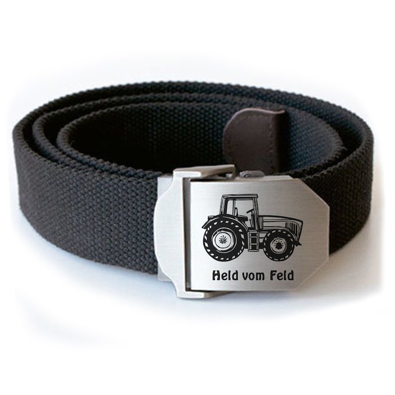 Op de afbeelding: Een zwarte canvas riem met een zilveren gesp met een tractorsilhouet en de tekst "Held vom Feld".