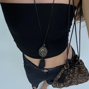 May include: A black tube top and shorts are worn with a long black necklace with a beaded pendant and tassel. A small drawstring bag with a gold and black pattern hangs from the shoulder.
