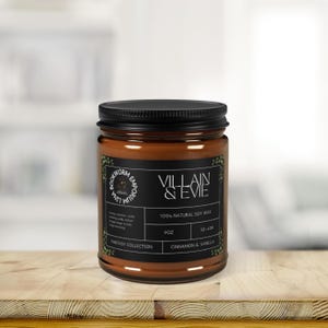 Könnte beinhalten: Eine braune Glas-Kerze mit schwarzem Deckel. Das Etikett lautet "VILLAIN & EVIE" und "CINNAMON & VANILLA". Die Kerze gehört zur "FANTASY COLLECTION" und enthält 255g 100% natürliches Sojawachs mit einer Brenndauer von 50-60 Stunden.