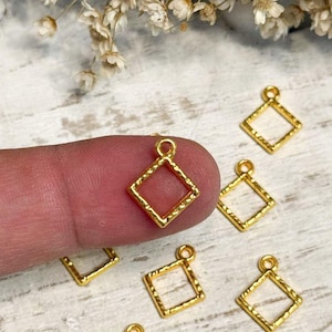 May include: A collection of small, gold-colored square charms with a textured, hammered finish. Each charm features a hollow center and a small loop at the top for attachment. The square frames are uniform in design and metallic appearance.