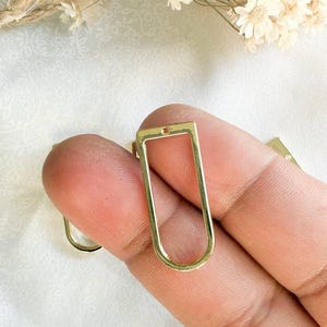 May include: Gold-toned metal rectangle pendant with a hole at the top. The pendant has a rounded rectangular shape with a smooth finish.