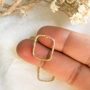 May include: A gold square pendant necklace with a textured finish. The necklace is on a chain with a delicate, textured design.