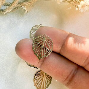 May include: Gold leaf-shaped metal charms with a delicate, intricate design. The charms have a hole at the top for attaching to jewelry or other crafts.