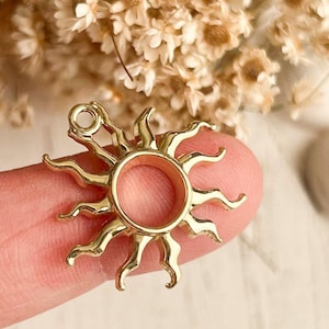 May include: Gold-toned metal sun charm with a round opening in the center. The sun has a detailed design with rays extending from the center.