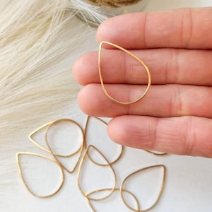May include: A close-up of a group of gold teardrop-shaped wire loops. The loops are arranged in a random pattern on a white surface.