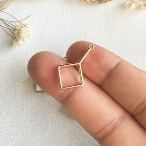 May include: Gold-toned metal square frame pendant with a loop at the top. The frame is open on all sides.