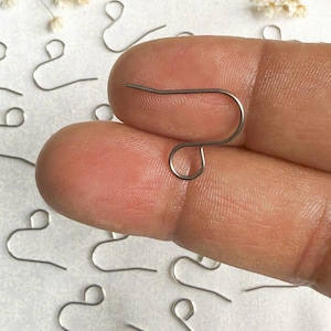May include: Silver-toned earring hooks, also known as ear wires, are shown in a close-up image. The hooks are made of metal and have a simple, classic design. They are commonly used for making earrings.