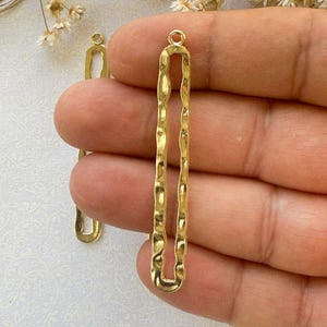 May include: Two gold-toned metal earring blanks with a textured, wavy design. The blanks are long and narrow, with a loop at the top for attaching earring wires.