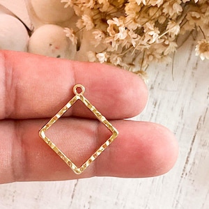 May include: Gold-toned metal pendant in the shape of a diamond with a textured surface. The pendant has a loop at the top for attaching to a chain or cord.