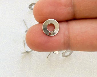 May include: Silver earring findings with a round shape and a small hole in the center. The findings are shown on a finger.