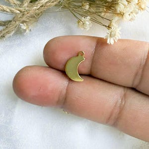 May include: A gold-colored crescent moon charm pendant. The charm is small and delicate, perfect for adding a touch of whimsy to jewelry.