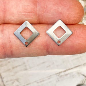 May include: Two silver diamond-shaped metal charms with a small hole at the bottom. The charms are about 1 inch in size.