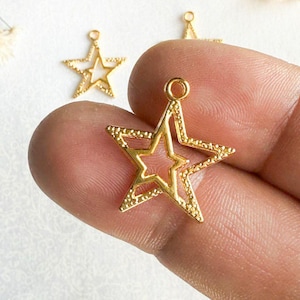 May include: Gold-toned metal star charm with a smaller star cut out in the center. The star has a textured surface.