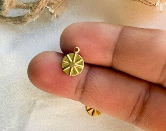 May include: Two gold-colored metal charms with a circular shape and a sunburst design. The charms have a small loop at the top for attaching to jewelry or other crafts.