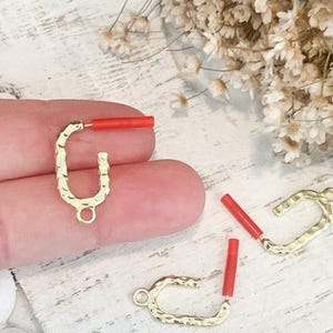 May include: Three gold-toned metal hoops with a hammered texture. Each hoop has a small loop at the top and is paired with a red, cylindrical bead.
