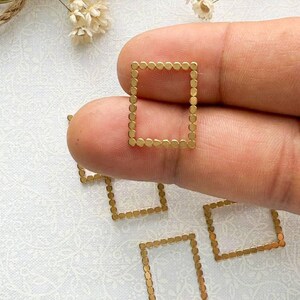 May include: Gold-toned metal square frames with a dotted border. The frames are small and delicate, perfect for adding a touch of elegance to jewelry projects.
