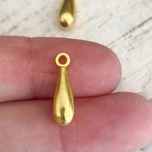 May include: Two gold teardrop shaped charms with a loop at the top for attaching to jewelry.