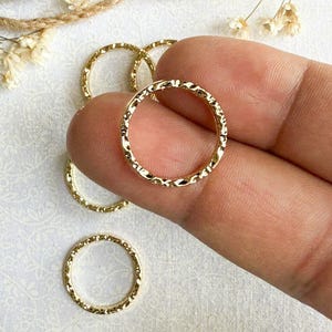 May include: A set of four gold-toned metal rings with a textured surface. The rings are stacked on top of each other.