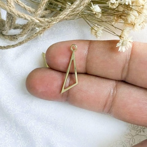 May include: Gold-toned metal triangle pendant with a small loop at the top. The pendant has a geometric design with an open center.