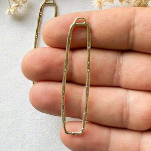 May include: Two gold-toned metal rectangular frames with a textured surface. The frames have a loop at the top for hanging.