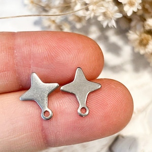 May include: Two silver star-shaped charms with a loop at the bottom. The charms are on a finger.
