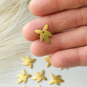May include: Gold metal star-shaped beads with a hole in the center. The beads are about 1 cm in diameter and have a textured surface.