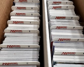 May include: A white box with two sections, each filled with stacks of Magic: The Gathering trading cards. The cards are organized alphabetically by letter, with dividers labeled A through Z.