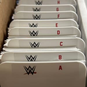 May include: A close-up of a white card catalog drawer with black and white WWE logos and red letter labels from A to H.