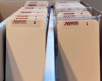 May include: A close-up of a white card holder with a Magic: The Gathering logo and the letter "A" on the front. The card holder is in a white plastic container with other card holders.