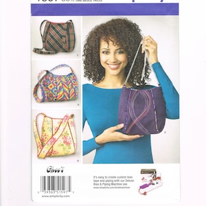 May include: Simplicity sewing pattern 1597 featuring various bag designs. The pattern includes images of bags in different styles, including a plaid shoulder bag, a colorful patterned bag, and a floral print bag. The model is holding a purple bag.