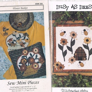 May include: Two quilting patterns, one titled "Flower Basket" and the other titled "Busy As Bees". Both patterns feature a yellow background with a white center and are surrounded by a brown border. The "Flower Basket" pattern shows a pillow with a flower basket design and the "Busy As Bees" pattern shows a beehive with bees flying around it.