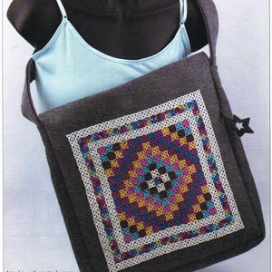May include: A gray fabric messenger bag with a white crocheted square design in the center. The design features a variety of colors including pink, blue, yellow, and brown.