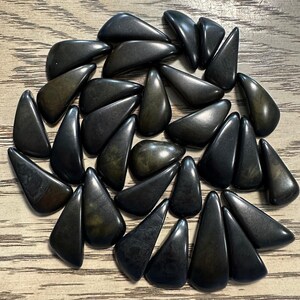 May include: A collection of black and green gemstone chips, each with a unique shape and texture. The chips are arranged in a circular pattern on a wooden surface.