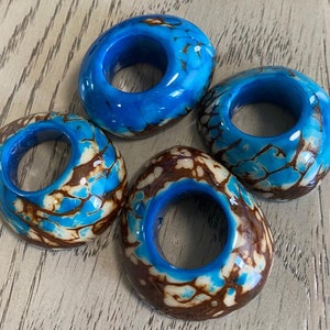 Könnte beinhalten: Vier blaue und braune gemusterte Keramikringe mit einem Loch in der Mitte. Die Ringe sind aus einem glatten, glänzenden Material gefertigt und haben ein einzigartiges Marmormuster.