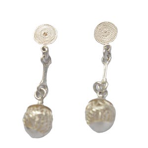 Puede incluir: Un par de pendientes de plata con un disco redondo texturizado en la parte superior y una bola redonda texturizada en la parte inferior.