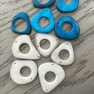 May include: A collection of nine irregularly shaped beads. The beads are in shades of blue and white, with a hole drilled through each. The beads have a smooth, polished appearance and are likely for jewelry making or crafts.