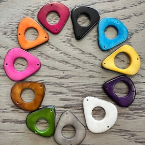May include: A collection of colorful, teardrop-shaped beads with a circular hole in the center. The beads are arranged in a circular pattern and come in various colors, including orange, pink, black, blue, yellow, purple, brown, green, gray, and white.