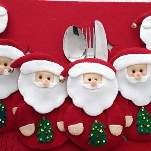 Könnte beinhalten: Sechs rote Filz-Weihnachtsmann-Platzkartehalter mit weißen Bärten und grünen Filz-Weihnachtsbäumen. Die Halter befinden sich auf einem roten Filz-Hintergrund.