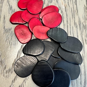 May include: A set of 15 black and 15 red game pieces made of wood. The pieces are oval shaped and have a smooth, polished finish.