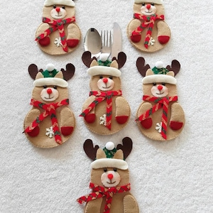 May include: Six felt reindeer place card holders with red and green accents. Each reindeer has a red scarf and a white snowflake on its belly.