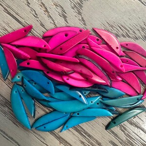 May include: A collection of crescent-shaped beads in vibrant shades of hot pink and bright turquoise. Each bead features a smooth, curved design with a small, pre-drilled hole near one end, suitable for jewelry making and various craft projects.