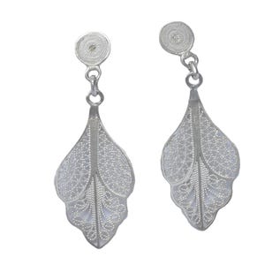 Puede incluir: Un par de pendientes de filigrana de plata con un diseño de hoja. Los pendientes son delicados e intrincados, con un pequeño disco redondo en la parte superior.