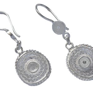Puede incluir: Un par de pendientes de filigrana plateados. Cada pendiente presenta un diseño circular con detalles intrincados y un borde texturizado. Los pendientes tienen un cierre de gancho y se muestran sobre un fondo blanco.