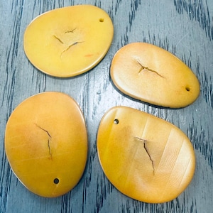 May include: Four yellow, oval-shaped, natural, polished, smooth, organic,  decorative,  stone pendants with a hole at the top. Each pendant has a crack or line running through it.