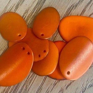 Könnte beinhalten: Eine Gruppe von acht orangefarbenen, ovalen Kunststoffpailletten mit einem Loch in der Mitte. Die Pailletten liegen auf einer Holzoberfläche.